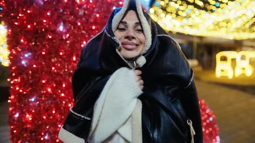 Woman Puts on Jacket in Front of Christmas Lights