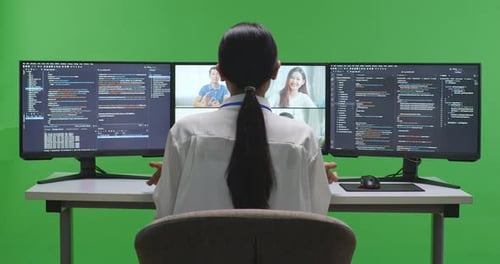 Entwicklerin hat Video, während sie Code mit mehreren Computerbildschirmen im Green Screen Studio schreibt