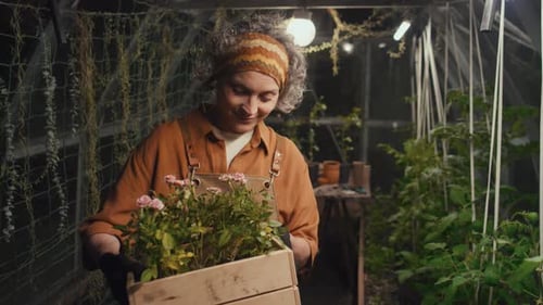 Woman Gardening with Flowers in Greenhouse at Night