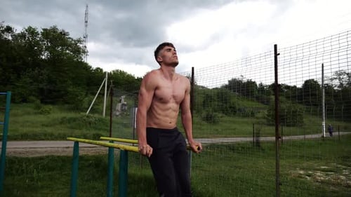 Strong Man Trains Abdominal Muscles Raising Legs on Parallel Bars at Sports Ground Young Shirtless