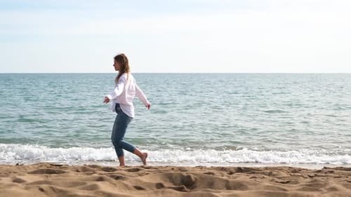 Summer vacation, young adult woman in white linen shirt walking on sea beach