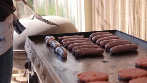 Cooking meat on a barbecue hotplate outside with sausages and hamburgers on a warm sunny day for lun