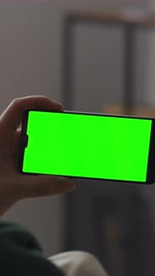 Person Holding Smartphone with Bright Green Chroma Screen in Cozy Indoor Setting Displaying Blank