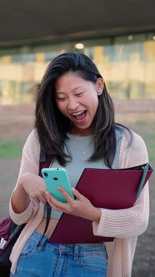 Jeune fille chinoise verticale souriant en regardant son téléphone portable penché sur le campus universitaire