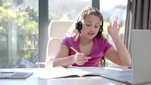 Happy biracial girl using headphones and laptop for online school lesson at home