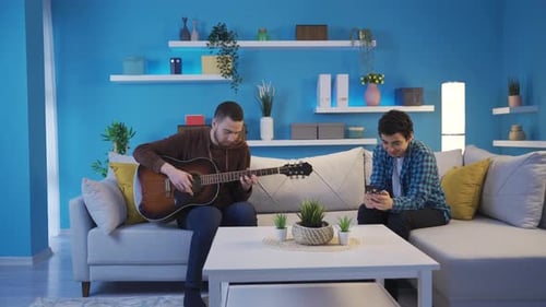 Man Playing Guitar for Friend on the Couch