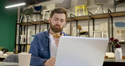 Man Eating a Sandwich While Working on Laptop