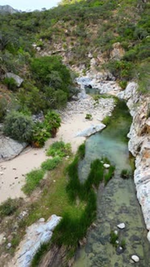 Aerial drone view of a narrow canyon river with crystal green water flowing between rocks and desert