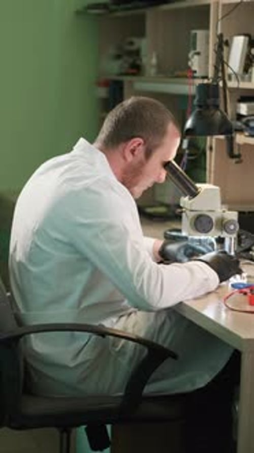 Man in Lab Coat Uses Microscope