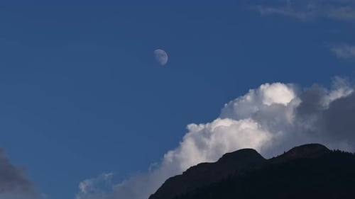 Daytime Moon Hanging in the Blue Sky Over a Mountain Silhouette