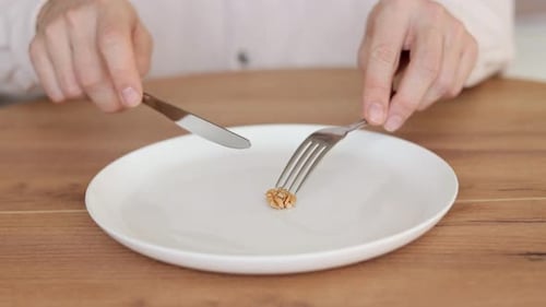 Person Cuts Walnut on Plate with Knife and Fork