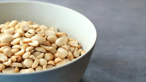 Bowl of Shelled Peanuts with Hand Reaching In
