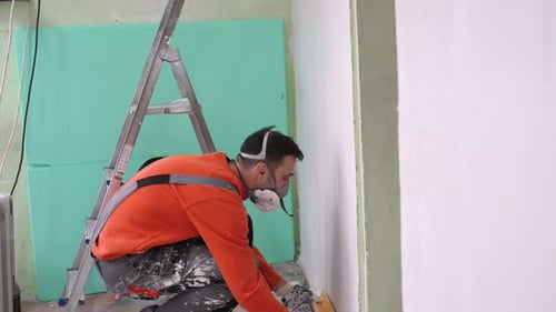 Man smoothing plaster on wall wearing safety mask