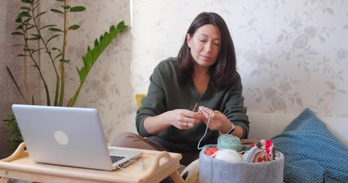 Woman Crocheting at Home with Laptop Nearby