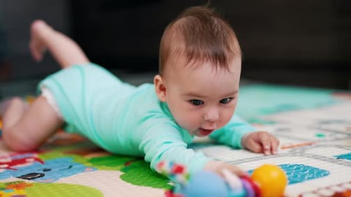 Sweetest child in blue outfit tries to reach his toy. Funny toddler takes a toy and shakes it.