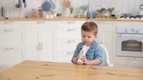Cute Baby Toddler Drinks Milk or Yogurt or Kefir in the Light Cozy Kitchen Handsome Caucasian Boy