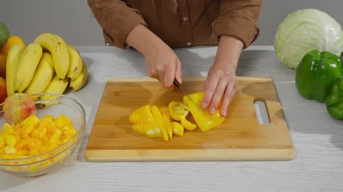 Hands chop yellow bell pepper on cutting board