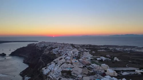 Aerial late sunset over Oia, Santorini, Greece, flying straight over white buildings, no clouds.