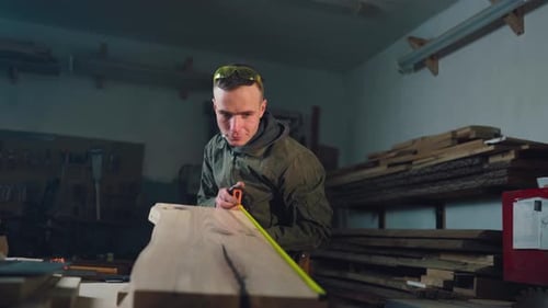 Man Measures Wood in Workshop with Tape Measure