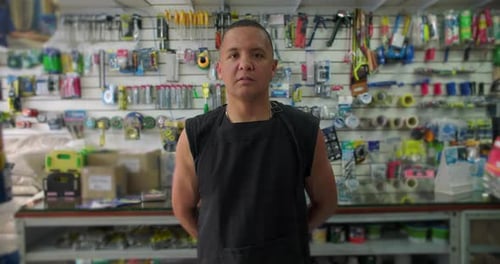 Hispanic hardware store worker standing among tools with serious expression conveying focus