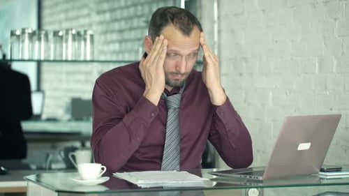 Stressed man in office with headache and laptop