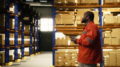 African American Worker Reviewing Inventory Data in Warehouse Distribution Hub