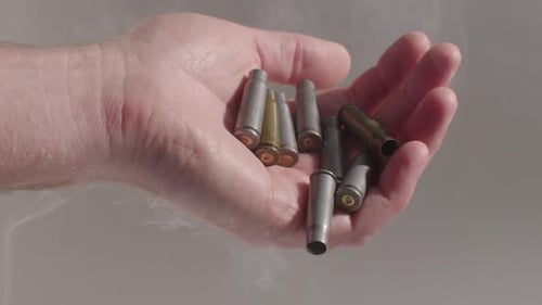 Nahaufnahme einer Handvoll Patronen in Zeitlupe, die weggeworfen werden, während Rauch herumweht.