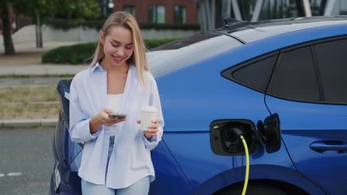 Blonde Woman Texts on Smartphone While Electric Car Charging