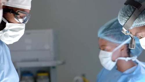 Diverse surgeons wearing surgical gowns operating on patient in operating theatre, slow motion