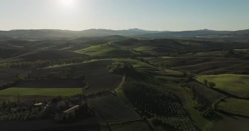 Aerial view of rolling hills and fields under a serene sky, Italy.