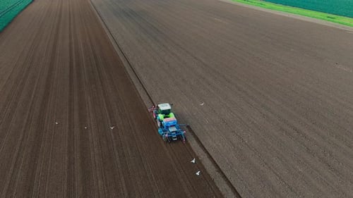 Aerial view of a green tractor plowing a field, cultivating land with a spike tooth harrow cutting,