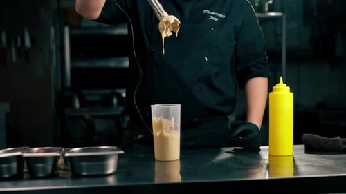 in a Professional Kitchen a Chef Prepares a Sauce for Salad Beats It with a Mixer Adding Ingredients
