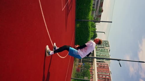 A tall guy basketball player throws a ball into a basketball hoop at a basketball court in the park