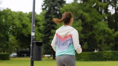 Smiling woman running along park in slow motion for fitness and healthy lifestyle