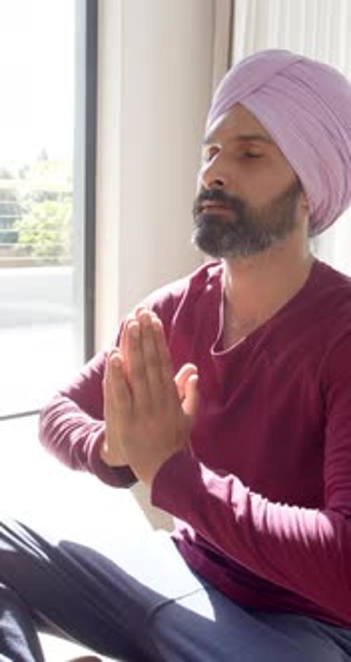 Vidéo verticale : Méditant à la maison, homme au turban pratiquant la pleine conscience dans le salon