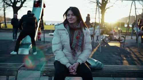 Peaceful happy 30s woman seated at playground bench gazing in contemplation and quiet solitude.