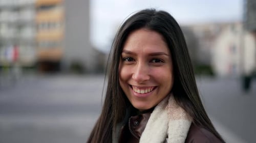 Portrait of a happy Middle Eastern young woman smiling at camera standing in city street. Closeup
