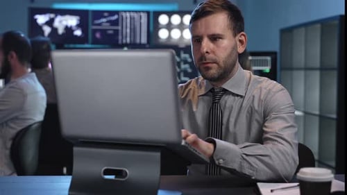 Männlicher Händler sitzt am Schreibtisch im Büro und arbeitet am Laptop, überwacht die Börse und schaut auf Monitore