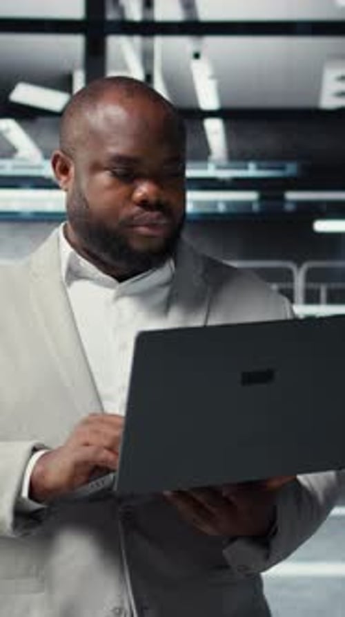 Vertical Video Technician Walking in Data Center Using Laptop to Check Hardware