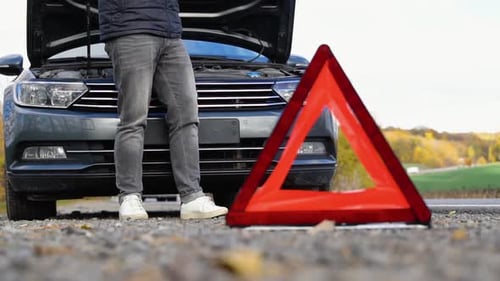 Road Side Warning Triangle Warning Oncoming Traffic of a Broken Down Car with a Man Using His Cell
