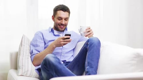 Man Relaxing on Couch Using Phone, Drinking Coffee