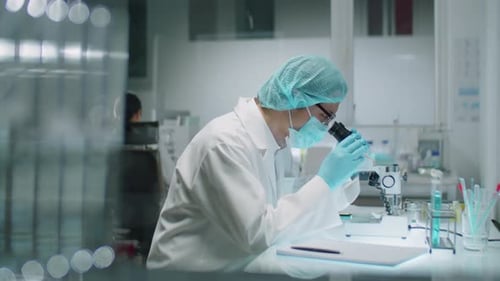 Scientist Looks Through Microscope and Writes Notes