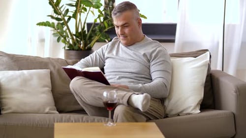 Man Reads Book and Drinks Red Wine at Home