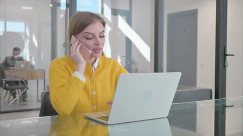 Woman Works on Laptop and Talks on Phone in Office