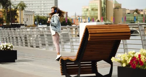 Urban Coffee Break Happy Young Woman Dancing While Walking Along the Embankment She is Listening to