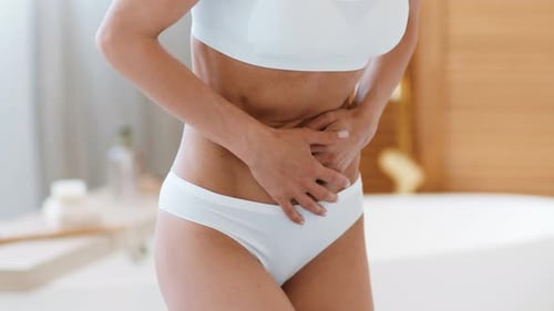 Frau mit heller Haut, die tagsüber ihren Bauch im Badezimmer hält