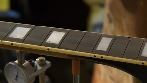 Un técnico de guitarra de cerca aplica relleno en un diapasón de guitarra de ébano