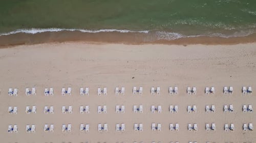A Sandy Beach Stretches Along the Seaside Adorned with Empty Sun Loungers Aerial View