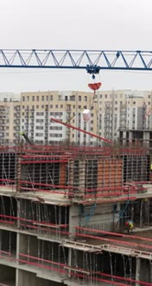 Vertical Aerial Drone View of Tower Crane Lifting Construction Materials Over Residential Building S