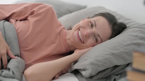 Smiling Young Woman Looking at Camera while Lying on Side in Bed